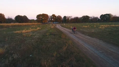 Three kids riding bikes on a path leading towards their village from the high Stock Footage 113098424