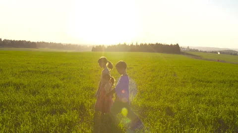 Three kids walking in a green field with the sunset in the background Stock-Footage 59180440
