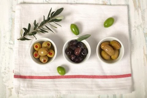 Three kind of olives and young olive branch on cloth napkin over old wood bac Stock Photos