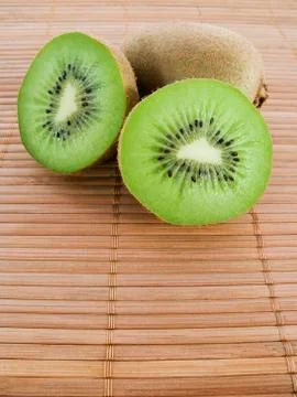 Three kiwis over a bamboo mat Stock Photos