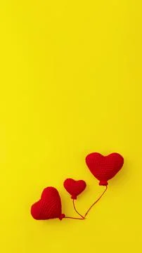 Three knitted red heart-shaped balloons in row on yellow background, concept  Stock Photos