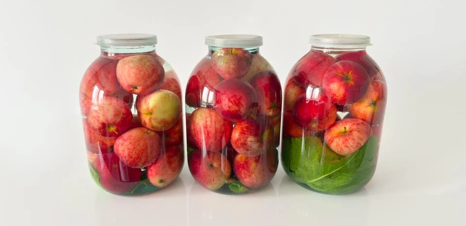 Three large glass jars with fermented pickled red apples and green leaves Stock Photos