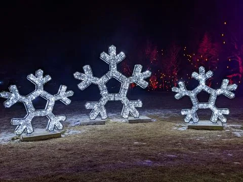 Three Large Glowing Snowflake Light Sculptures in a Winter Night Landscape Foto stock