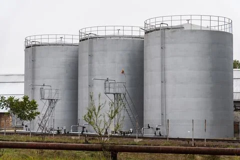 Three large, gray cylindrical storage tanks are positioned Stock Photos