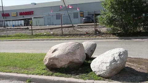 Three large gray rocks sitting on grass traffic island with parking lot Stock Footage 249098098