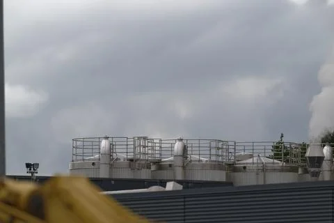Three large industrial silos with black roofs lights and smoke under cloudy s Stock Photos