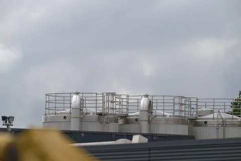 Three large industrial silos connected by pipes and ladders under cloudy sky Stock Photos