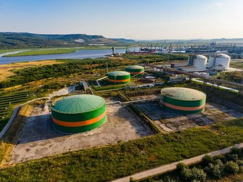 Three large storage tanks sit on a flat area near a river. Industrial buildin Stock Photos