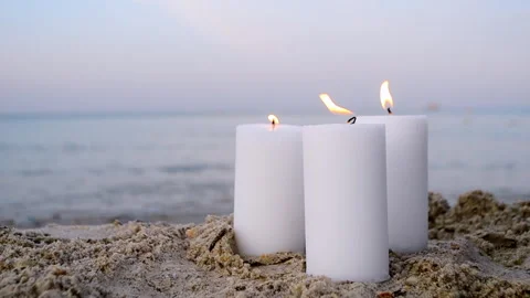 Three large white paraffin candles burn on sand beach on background of sea waves Stock Footage 167628505