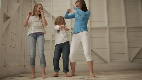 Three laughing sisters dancing while standing next to each other in a garage. 스톡 동영상 88341864