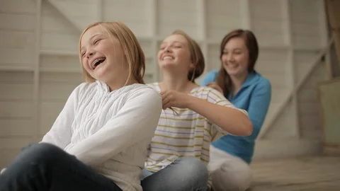 Three laughing sisters having fun playing with each others hair while sitting in Vídeo Stock 88341866