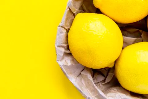 Three lemon on yellow background. Group of fresh lemon in recycling paper bag. Stock Photos