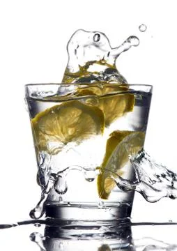 Three lemons are falling into the glass of water. Stock Photos