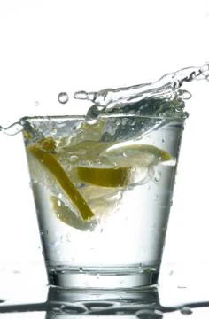 Three lemons are falling into the glass of water. Stock Photos