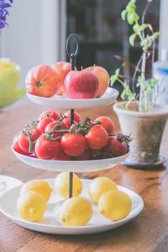 Three-level plate with apples, tomatoes, and lemons on it in the kitchen Stock Photos