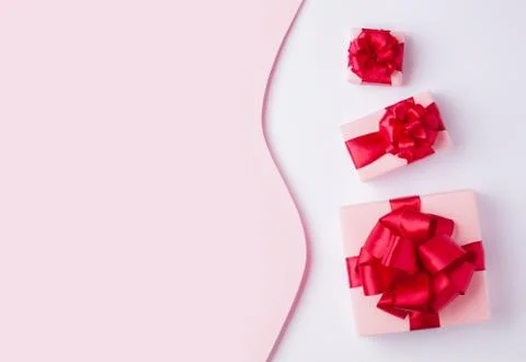 Three light pastel pink boxes tied with a red satin ribbon. Stock Photos