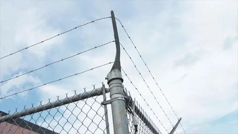 Three lines of barbed wire at top of silver fence corner with sky behind Stock Footage 249752313