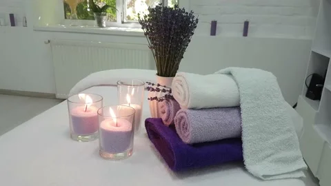 Three lit candles, rolled lavender colored towels in a massage parlor Stock Footage 156901556