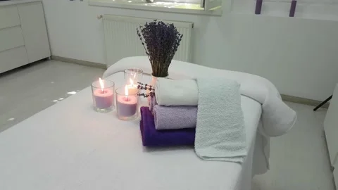 Three lit candles rolled lavender colored towels  in a massage parlor Stock Footage 156901567