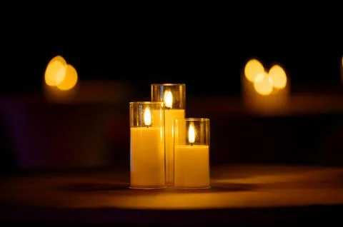 Three lit candles on a table with blurred background lights Stock Photos