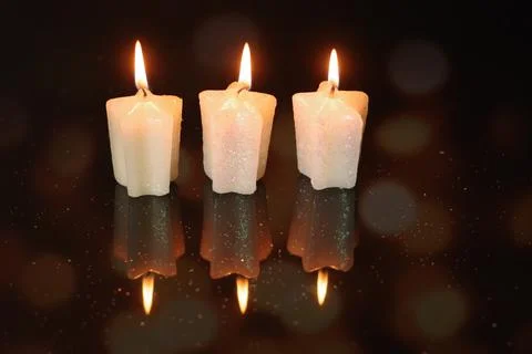 Three lit star candles with a reflective black surface with blurred lights Stock Photos