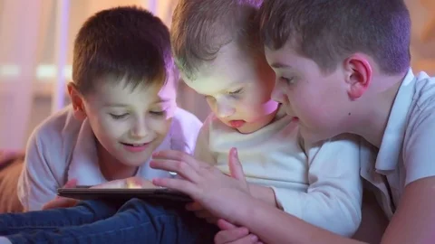 Three little boys with tablet computer in a dark room. Kids playing games on tab Stock Footage 73750279