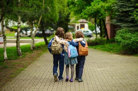 Three little school students, two boys and the girl, go in an embrace to scho Stock Photos