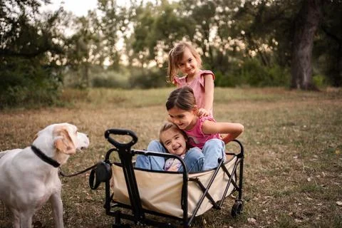 Three little sisters having fun with their dog in a wagon in a park Stock Photos