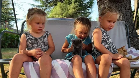 Three little sisters triplets sitting in the yard with kittens in their arms 库存影片 266290258