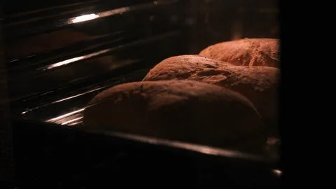 Three loaves of bread are baked in the oven. The light inside the oven Stock Photos