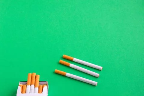 Three loose cigarettes next to a pack on the green table Stock Photos