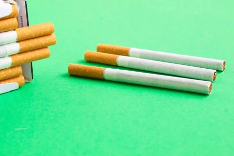 Three loose cigarettes next to a pack on the green table Foto stock