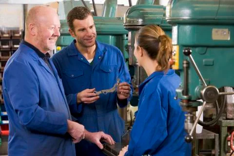 Three machinists in workspace by machine talking Stock Photos