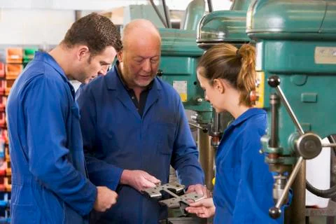 Three machinists in workspace by machine talking Stock Photos