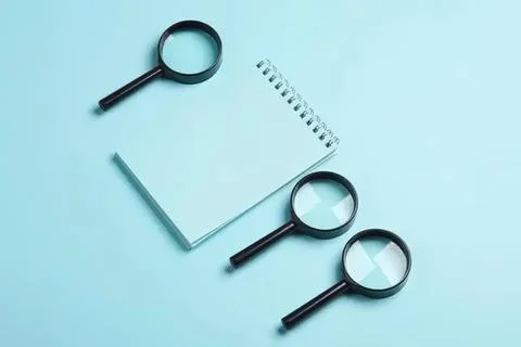 Three magnifying glasses and notebook on blue background Stock Photos
