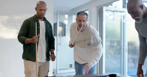 Three male friends at pool table watching cream-sweater man striking cue ball to Stock-Footage 342068575