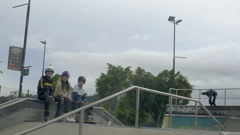 Three males jump and spin at skatepark while three other people watch and Stock Footage 171491764