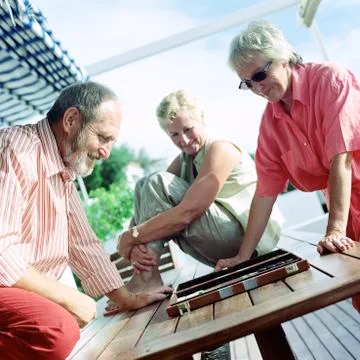 Three mature adults playing backgammon Stock Photos