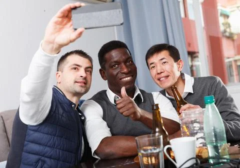 Three men are looking in mobile and taking selfie together 스톡 사진