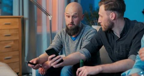 Three men are relaxing on couch in living room in evening in front of the TV Stock Footage 160440038