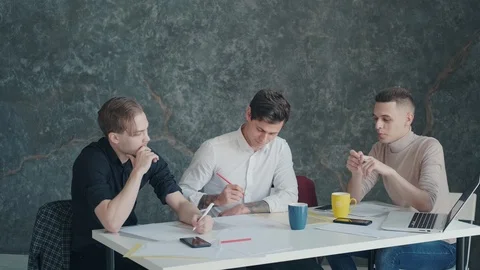 Three men discuss a project and plan while sitting at a table in an office Stock Footage 119110348