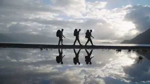 Three Men Hiking Past Their Reflections On Calm Water At Sunset Stock Footage 70449980