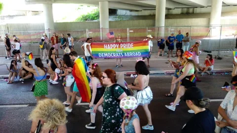 Three men hold a large rainbow flag and an American flag in front of people Stock Footage 197372223