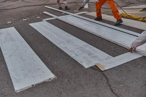 Three men in orange work clothes are painting a crosswalk Stock Photos
