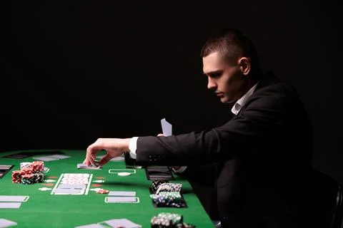 Three men play poker with chips and cards on a green table in a dark, smoky c Photos