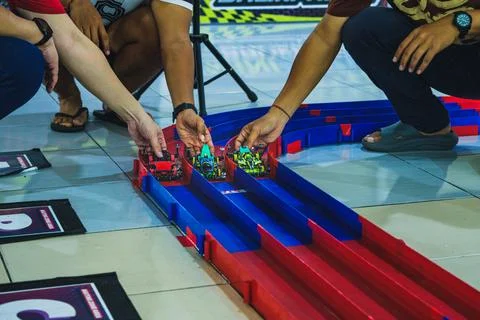 Three men playing with mini 4WD toy cars on a plastic racing track Stock Photos
