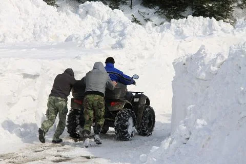 Three men push an ATV through a narrow path carved in deep snowbanks Stock Photos