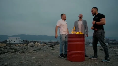 Three men stand by a barrel of fire on the outskirts of the city Stock Footage 151647747