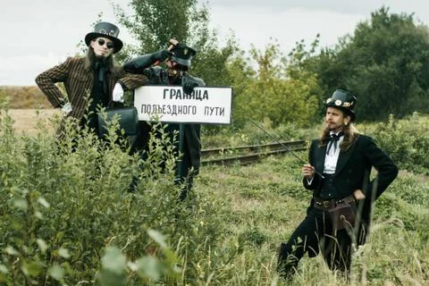 Three men in steampunk suits pose near an abandoned railway Stock Photos