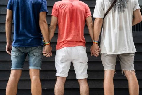 Three men on their backs holding hands with an lgtb flag bracelet Stock Photos